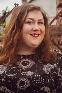 A person in a black dress and wearing red lipstick standing in front of a brick wall
