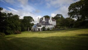 A large white house in sunlight surrounded by trees